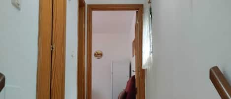 En hall med en röd soffa, en trädörr och en vit vägg med en telefon och en bilderam.