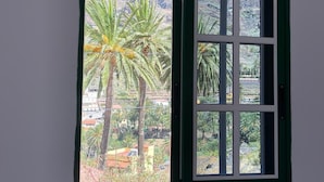 A room with a large window featuring a view of palm trees and a mountainous landscape. - Apartamentos Casa Rural Guadá (Valle Gran Rey)