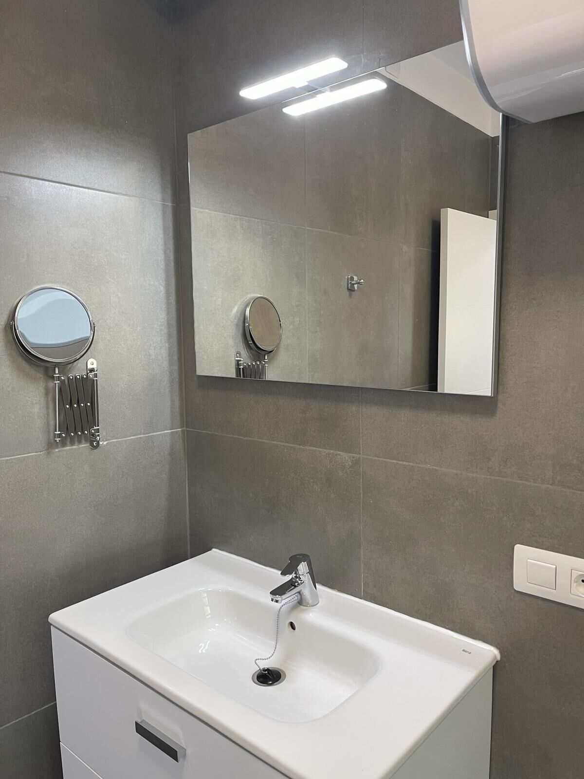 Un baño moderno con un lavamanos blanco, un espejo grande y un perchero para toallas.