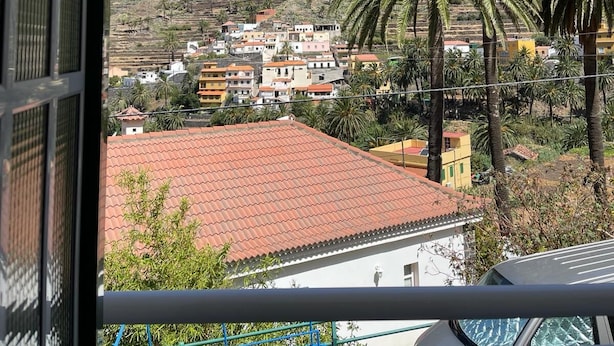 A balcony with a view of a hillside town, palm trees, and a mountain in the background. - Apartamentos Casa Rural Guadá (Valle Gran Rey)
