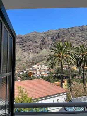 A balcony with a view of a hillside town, palm trees, and a mountain in the background.