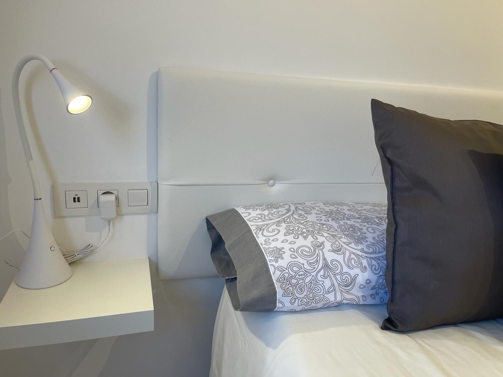 Une chambre d’hôtel bien rangée, avec un lit, une lampe de chevet et une prise de courant.