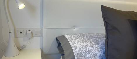 Une chambre d’hôtel bien rangée, avec un lit, une lampe de chevet et une prise de courant.
