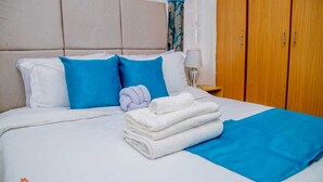 A hotel room with a bed, pillows, a folded towel, a nightstand, and a wardrobe. - Lux Suites Truna Executive Homes Kisii (Kisii)