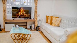 A living room with a flat-screen TV, a white sofa with yellow cushions, a wooden entertainment unit, and a small table with a tissue box. - Lux Suites Truna Executive Homes Kisii (Kisii)
