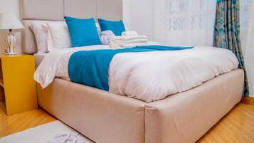 A neatly made bed with a beige headboard, blue and white bedding, and a pair of white towels on the side.