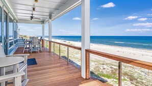 A covered deck with a view of the beach, wooden flooring, and a railing.