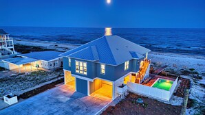 A two-story house with a large deck and a swimming pool, located near a beach.