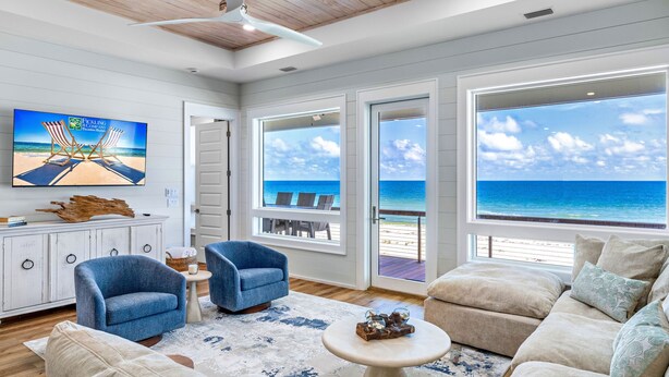 A spacious living room with a large TV, comfortable seating, and a view of the beach.