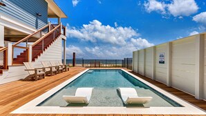 A swimming pool with wooden deck, lounge chairs, and a staircase leading to an upper deck.