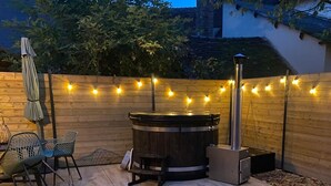 A wooden deck with a hot tub, string lights, and outdoor furniture.