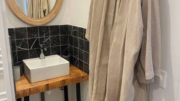 Une salle de bain avec un meuble-lavabo en bois, un lavabo blanc, des carreaux de marbre noir, un miroir rond et une serviette beige accrochée au mur.