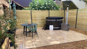 Un patio con mesa y sillas de madera, un jacuzzi y una chimenea.