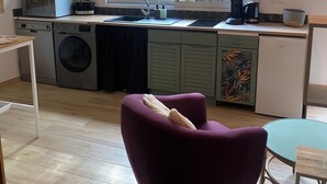 A compact kitchen with a washing machine, a microwave, and a sink. There is a window with a view of a garden.
