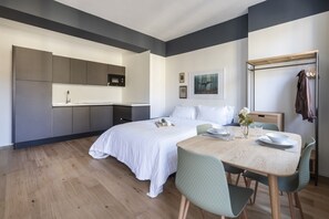 A modern bedroom with a large bed, a small kitchenette, a dining area with a table and chairs, and a clothing rack. - Easylife - Studio with balcony in Risorgimento (Milano)
