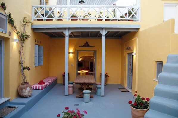 A yellow building with a covered patio area featuring a wooden table and benches, potted plants, and a staircase.