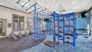 Uma academia com equipamentos azuis, uma TV fixada na parede e uma placa com o nome The Ranch Fitness Center.