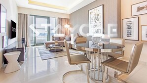 A modern hotel room with a dining area, a sofa, a TV, and a large window. - Staycae Holiday Homes - DAMAC Towers (Dubai)