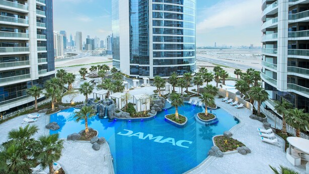 A modern hotel with a central pool surrounded by palm trees and lounge chairs. - Staycae Holiday Homes - DAMAC Towers (Dubai)