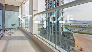 A modern apartment with a balcony, large windows, and a view of a tall building and highway. - Staycae Holiday Homes - DAMAC Towers (Dubai)