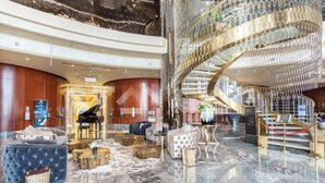 A luxurious lobby with a grand piano, plush seating, and a stunning spiral staircase. - Staycae Holiday Homes - DAMAC Towers (Dubai)