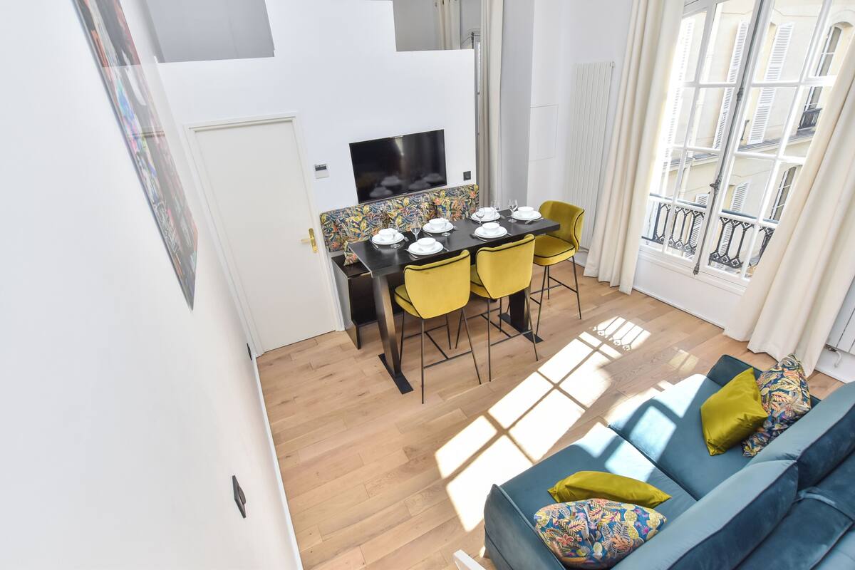 A modern living room with a blue sofa, yellow chairs, and a dining table set for four.