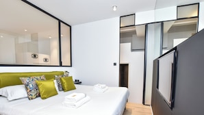 Una habitación de hotel moderna con una cama grande, cabecera verde y un espejo amplio.