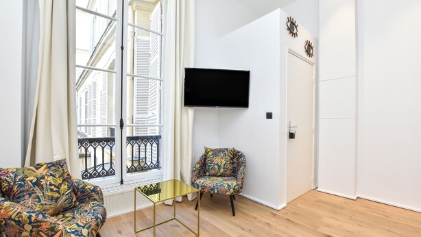 Una sala de estar moderna con un ventanal grande, un televisor de pantalla plana, un sillón estampado y una pequeña mesa de centro.