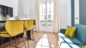Una sala de estar moderna con comedor, un sofá con cojín estampado y un ventanal con cortinas.