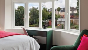 Un dormitorio con cama, escritorio y silla. Cuatro ventanas ofrecen vistas al exterior.