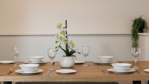 Una mesa de comedor dispuesta con cuencos, platos y copas de vino blancas, con una orquídea en maceta en el centro.