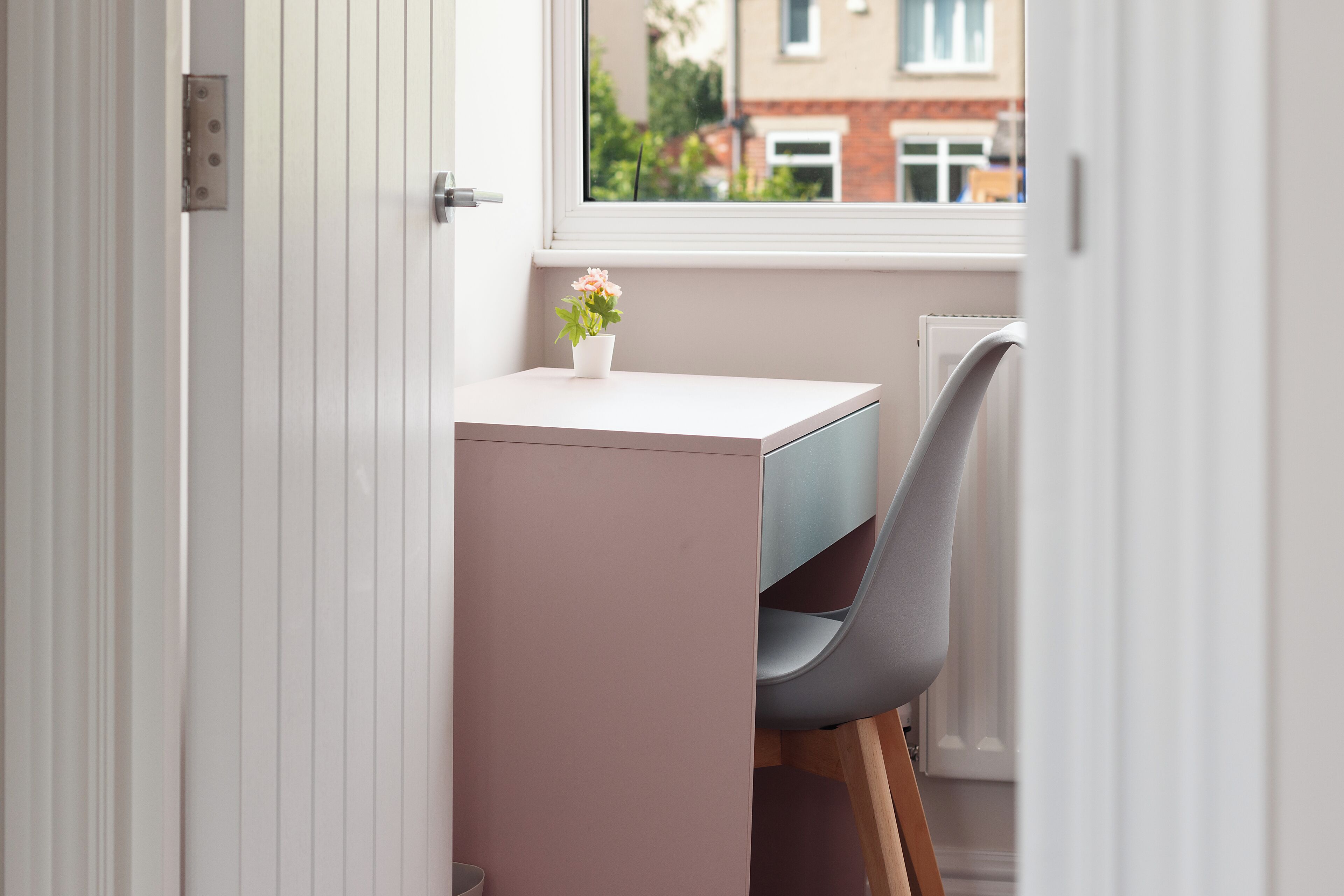 A small, private office space with a desk and chair, a potted plant, and a window with a view of buildings outside.
