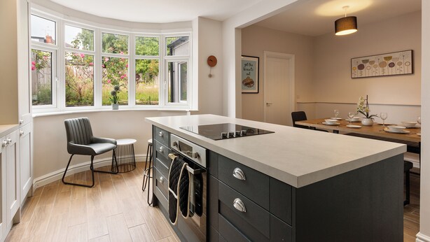 Una cocina moderna con un ventanal curvo, un comedor con una mesa dispuesta para cuatro personas y un horno empotrado.