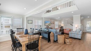 A spacious living area with a dining table, chairs, sofas, and a staircase. - Relax in this charming home in Holden Beach featuring 3 bedrooms. (Holden Beach)