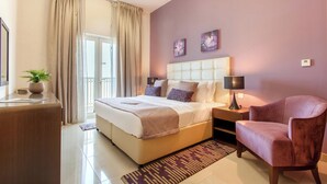 A modern hotel room with a large bed, a sitting area with a chair, a bedside table with a lamp, and a view of the outside through a window with curtains. - Staycae Holiday Homes - Suburbia (Dubai)