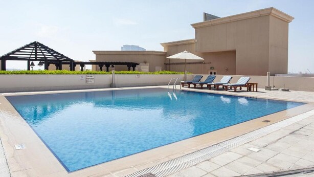 A rooftop pool with lounge chairs and a pergola. - Staycae Holiday Homes - Suburbia (Dubai)