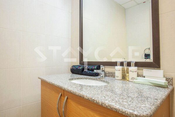 A bathroom with a granite countertop, a white sink, and toiletries. - Staycae Holiday Homes - Suburbia (Dubai)