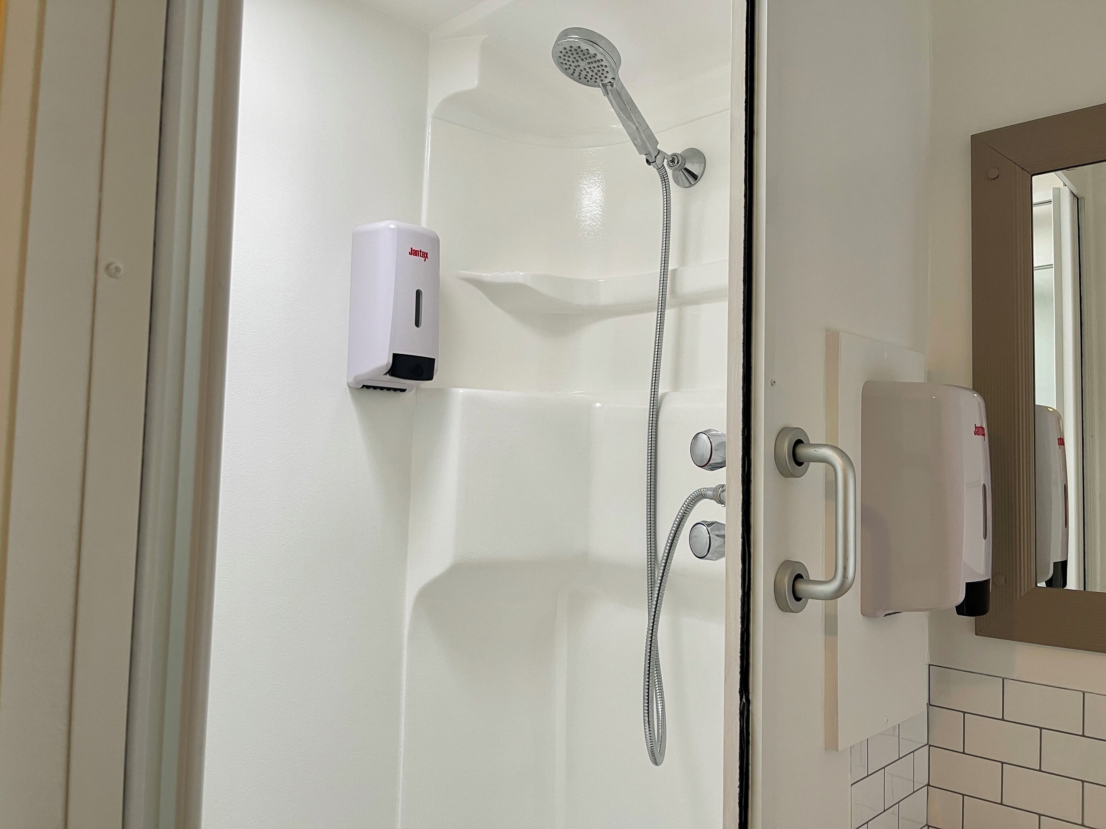 A shower area with a handheld showerhead, a handheld soap dispenser, and a towel rack.