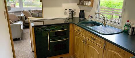 A compact kitchen with wooden cabinets, a built-in oven, a sink, and a window overlooking a garden.