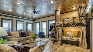 A spacious living room with a wooden ceiling, a sofa set, a coffee table, and a bunk bed with a ladder.