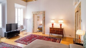 A spacious room with a television, a bed, a desk with lamps, and a chair. - Apartment located on the main floor of a historic building in the center of Rome (Roma)
