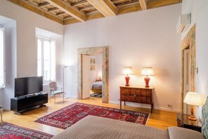 A spacious room with a television, a bed, a desk with lamps, and a chair.