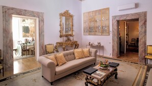 A living room with a sofa, a coffee table, a large mirror, and a painting on the wall. - Apartment located on the main floor of a historic building in the center of Rome (Roma)