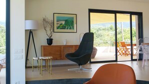 Una sala de estar moderna con un ventanal grande, una silla negra, una mesa de centro de madera y un cuadro en la pared.