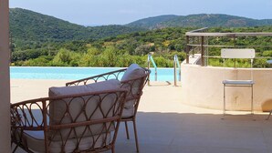 Una terraza con sillas de mimbre y vistas a una piscina y colinas.