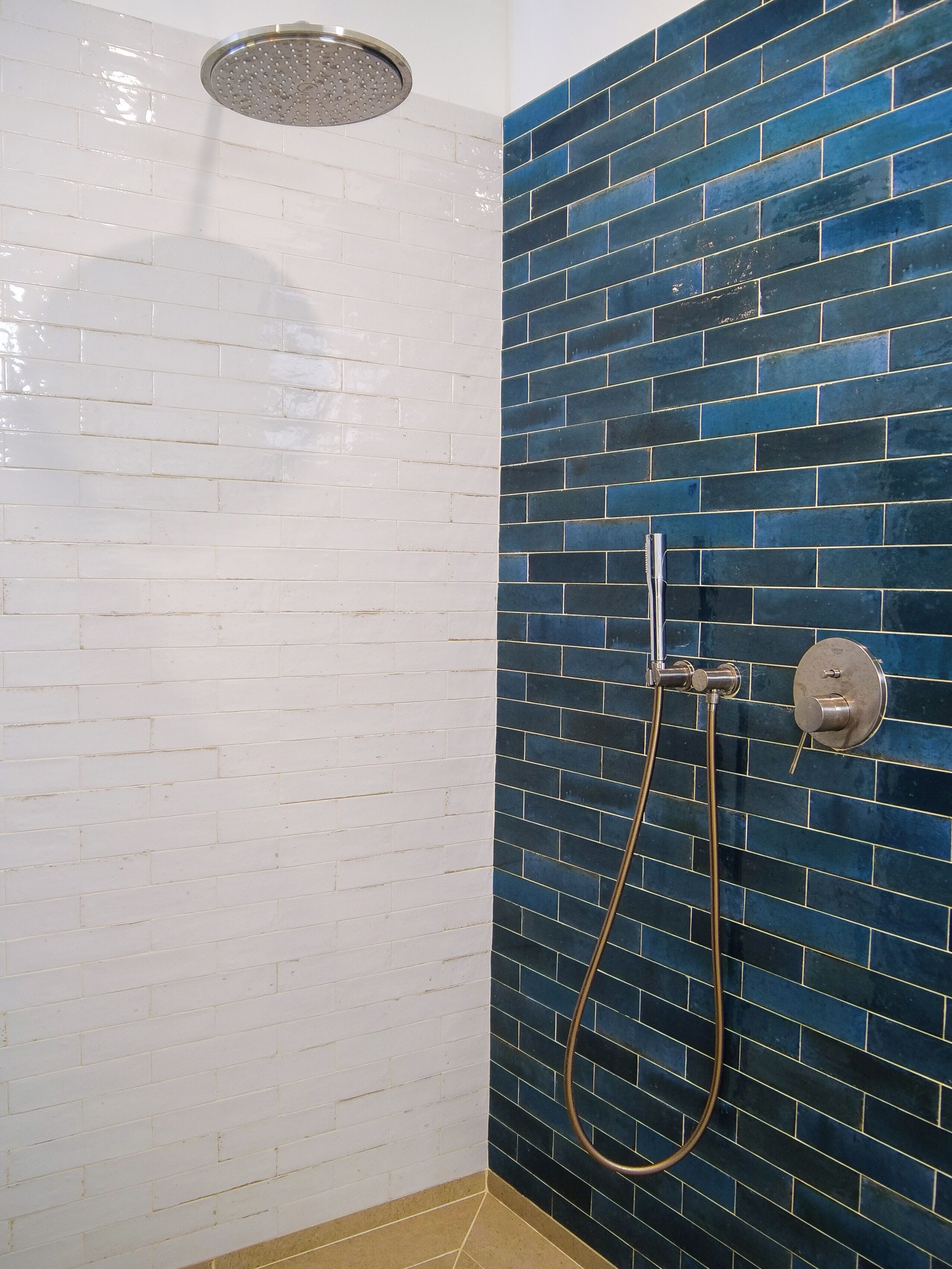 Une douche avec un mur recouvert de carreaux bleus et un sol recouvert de carreaux blancs.