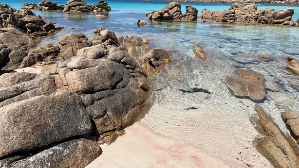 Una playa rocosa con aguas cristalinas y una vista distante de un paisaje montañoso.
