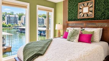 Een slaapkamer met een groot bed, uitzicht op een waterpartij en een groene wand.
