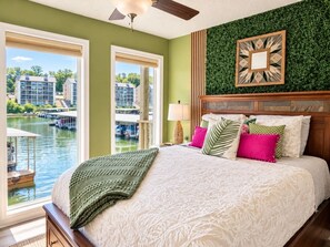 A bedroom with a large bed, a view of a water body, and a green wall. - Boho Flamingo-Pools, Hot Tub, Pet Friendly (Village of Four Seasons)