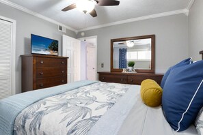 A bedroom with a bed, a dresser, a ceiling fan, a mirror, and a door leading to another room.